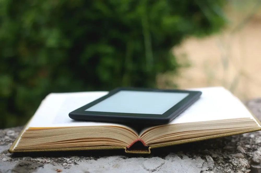 eReader laying on top of an open paper book outside on a cement ledge